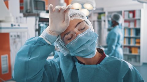 Indoor portrait young caucasian woman medical worker doctor professional nurse therapist wearing respiratory mask and blue uniform working in operating room.