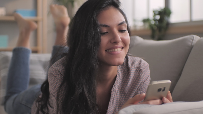 Happy smiling girl young woman lying on sofa video call friend using smart phone,female middle eastern mixed race millennial videocall speaks with relative distance communication concept | Shutterstock HD Video #1062956917