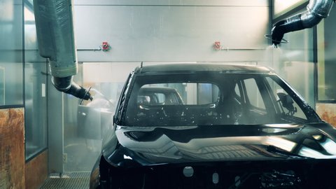 Car body being painted black by robotic arms