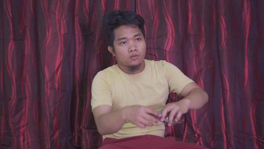 Young Asian man enjoying watching movie while eating snacks