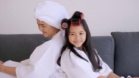 Mother with little daughter in bathrobes enjoying rolling hair together in living room.