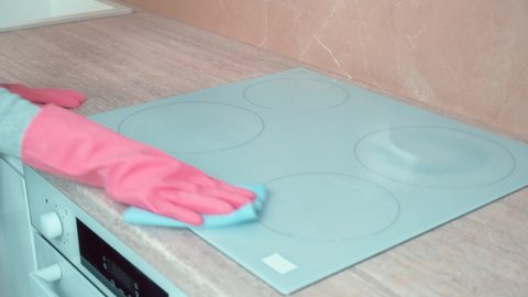 A female hand in gloves diligently does the cleaning in the kitchen, washes the surface of the stove. Cleaning the kitchen.
