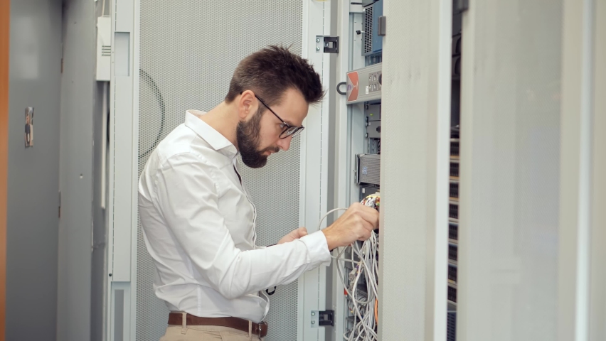 IT Technician Works With Ware And Cables in Big Data Center. Connecting Lan Cable To Mainframe.IT Engineer Patching Network Equipment In Server Room. Network Engineer Maintenance Work In Server Room Royalty-Free Stock Footage #1062962674