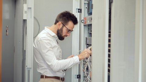 IT Technician Works With Ware And Cables in Big Data Center. Connecting Lan Cable To Mainframe.IT Engineer Patching Network Equipment In Server Room. Network Engineer Maintenance Work In Server Room