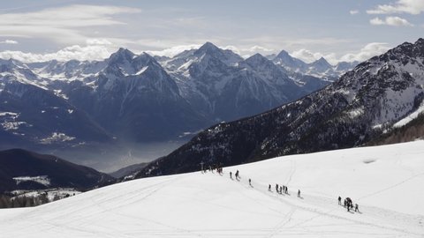 winter aerial view over group of people with snowshoes hiking down a snowy slope. In background magnificent snowy mountains. Mountains outdoor establisher.4k drone circle pan flight