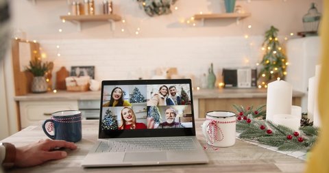 Close up. Rear of couple having multiple online video call on computer with happy multi-ethnic female and male friends sitting at decorated kitchen at home. New Year in social distancing in quarantine स्टॉक व्हिडिओ