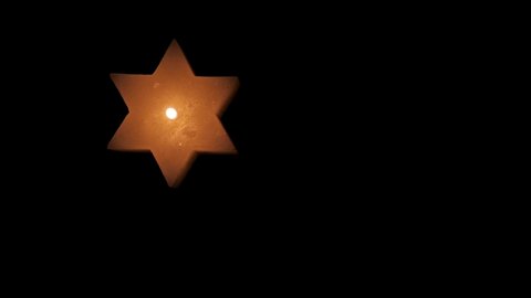 A lighted Jewish yellow candle in the shape of a star of David on Hanukkah. On a black isolated background close up in 4K without faces of people.