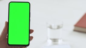 Close-up shot of green screen template smartphone in female hands at home offise, girl is watcing content, makes notes in a notebook. Modent technology and information concept.
