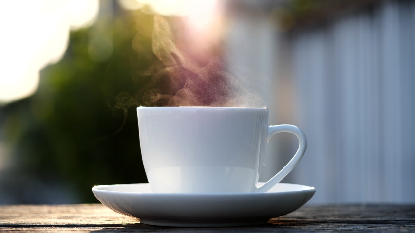 Close-up steaming hot coffee or tea cup, slow motion. Hot ceramic white coffee cup with smoke on old wooden table in nature background. Hot Coffee Drink Concept | Shutterstock HD Video #1062981541