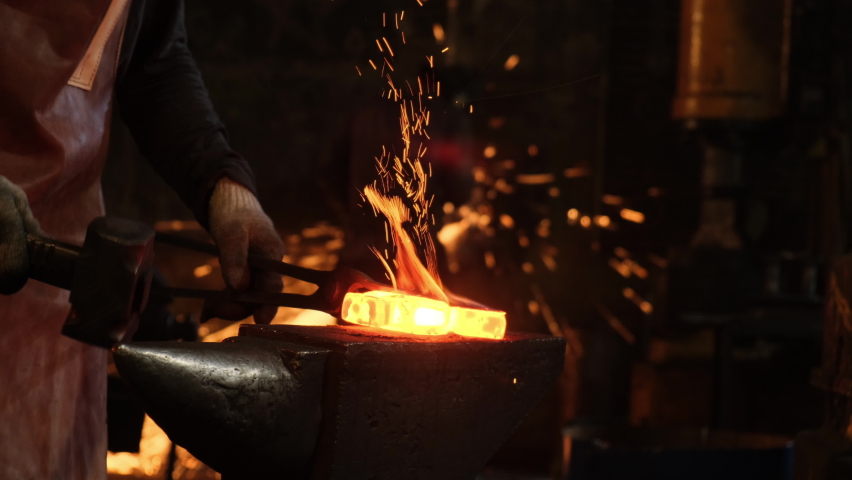 Medium shot of a man with a hammer hitting red-hot metal. A blacksmith works with metal in a forge. Sparks from impacts to metal | Shutterstock HD Video #1062983719