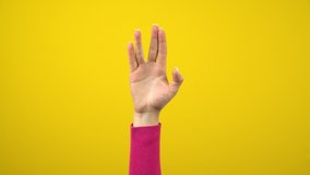 A female hand shows an alien greeting sign. Studio photography on an isolated yellow background. - Powered by Shutterstock - Get 15% off with code: PIKWIZARD15