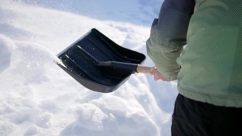 A man with a shovel removes snow. Sunny warm day, a lot of fresh snow after a blizzard. Cleaning the territory in winter