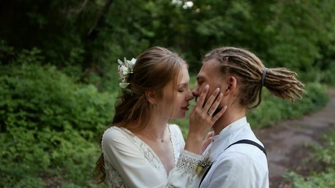young guy with dreadlocks and hipster girl kissing in the park. Wedding. Heterosexual couple of lovers caress each other in the park against the background of green colorful trees.