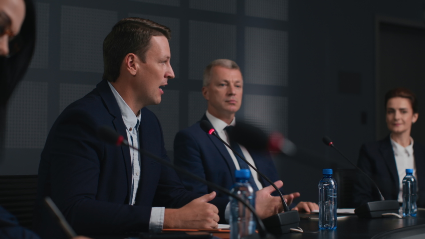 Political speaker talks at meeting room of modern business forum. Man in suit discusses partnership at conference in convention hall. Expert group of colleagues working together at official event Royalty-Free Stock Footage #1062994312