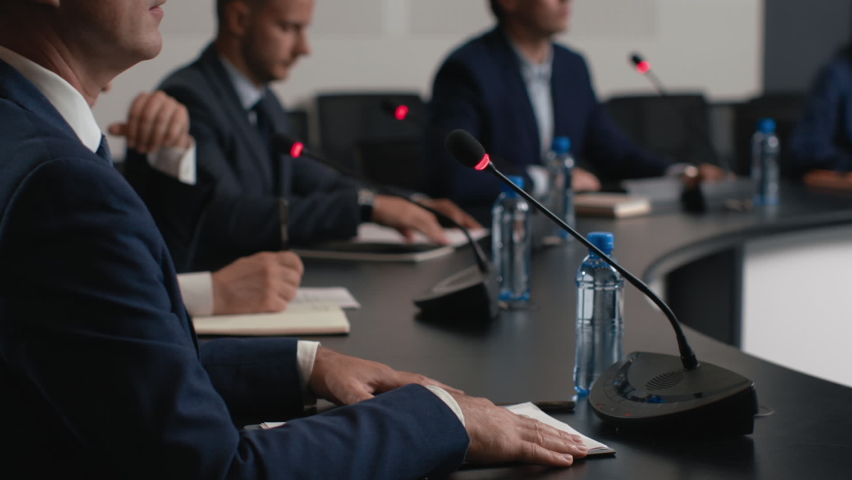 Political speaker talks at meeting room of modern business forum. Adult man in suit discusses partnership at conference in convention hall. Expert group of colleagues works at official event closeup Royalty-Free Stock Footage #1062994330