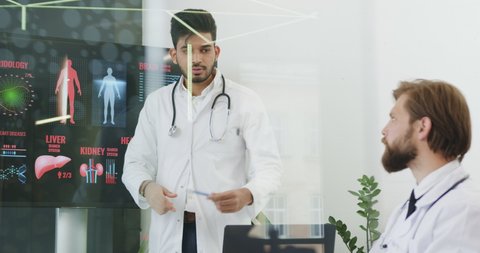 Medical concept where attractive confident experienced bearded medical worker holding a presentation on interactive monitor on risks heart desease theme in front of another colleagues