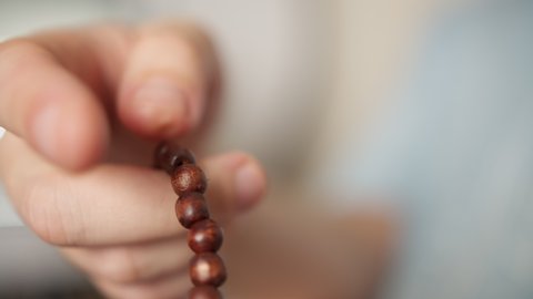 Man's hand with wooden rosary, goes through rosary, blurred background