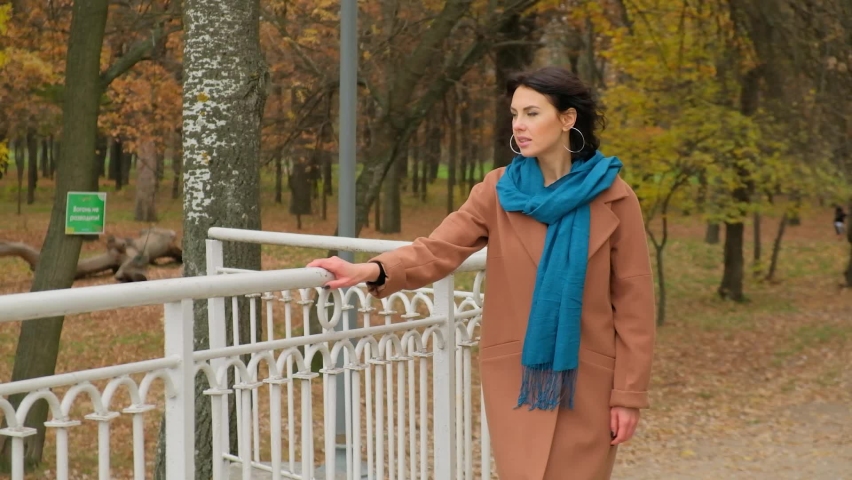 Young beautiful girl walks on the bridge in the park in the fall.