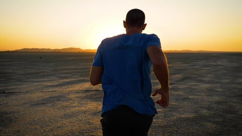 Athletic man working out with battle ropes on a dry lake at sunset.
