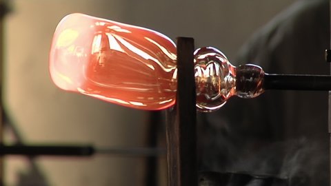 Glass Maker, Master Craftsman, shaping a red-hot Glass Bottle. Close Up.