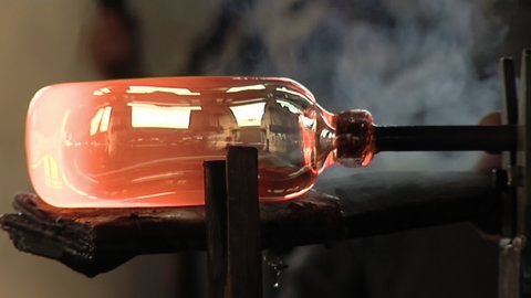 Glass Maker, Master Craftsman, shaping the End of a red-hot Vase. Close Up.