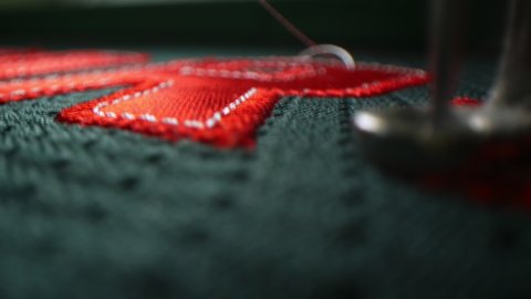 Automated machine tool embroiders red number on green fabric of hockey club uniform in sewing workshop extreme closeup