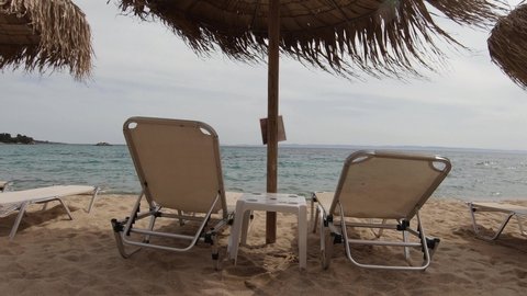 Exotic sun beds and umbrellas at a beach shore. View from the back with calm sea in the horizon.