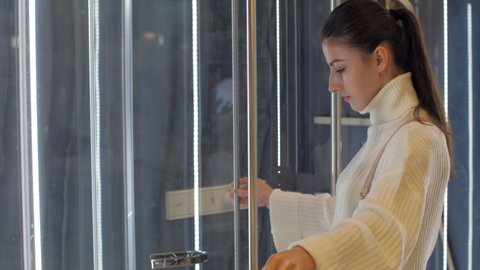 Professional designer in white pullover looks at transparent shower cabin door under electric light of hardware store. Concept designer work