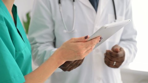 Closeup view of man and woman doctors using tablet during working day at clinic spbas. African American person and his female colleagues use electronic device and work together while standing indoors