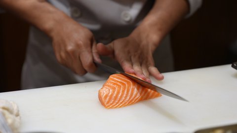 Close up of Professional male chef hand using fish fillet knife slice fresh orange salmon meat on cutting board in restaurant kitchen. Chef preparing healthy menu salmon sashimi or sushi to customer