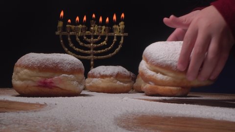Jewish family celebrates Hanukkah and eats doughnuts (Sufganiyot, Israeli Donuts). Holiday food on the table. The lights of the menorah burning candles