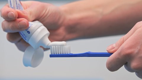 A woman in the bathroom squeezes white toothpaste from a tube onto a blue toothbrush on a white background, brushing her teeth, morning and evening procedures, hygiene