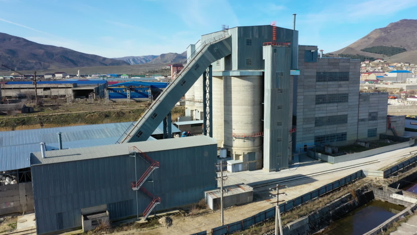 Large building on cement factory territory surrounded by low hills and big industrial town under blue sky close aerial view | Shutterstock HD Video #1063023037