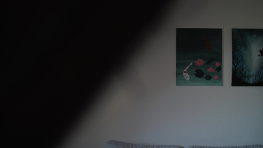 An attractive young woman walking in living room and looking outside of window. Bored and serious millennial girl during self quarantine at home in elegant top floor apartment with inclined walls.