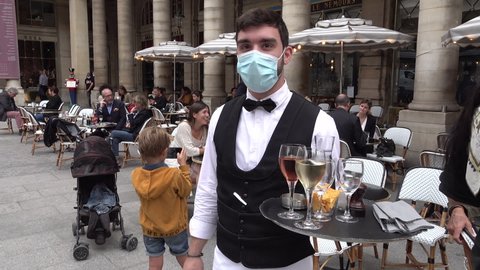 PARIS, FRANCE – SEPTEMBER 2020: Waiter wears protective face mask (and classic bow tie) serving wine and snacks on outdoor terrace of popular restaurant in central Paris, France. Covid-19 coronavirus 