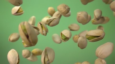 Close-up of salted pistachios flying down diagonally on a green background in slow motion