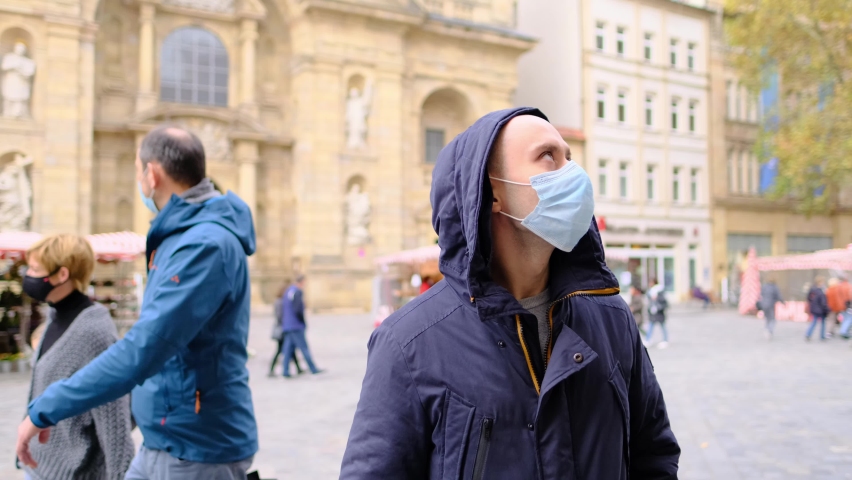 male tourist in a mask walks down the street, waiting in market square, architecture of old cities, travel concept, period of the covid-19 coronavirus pandemic