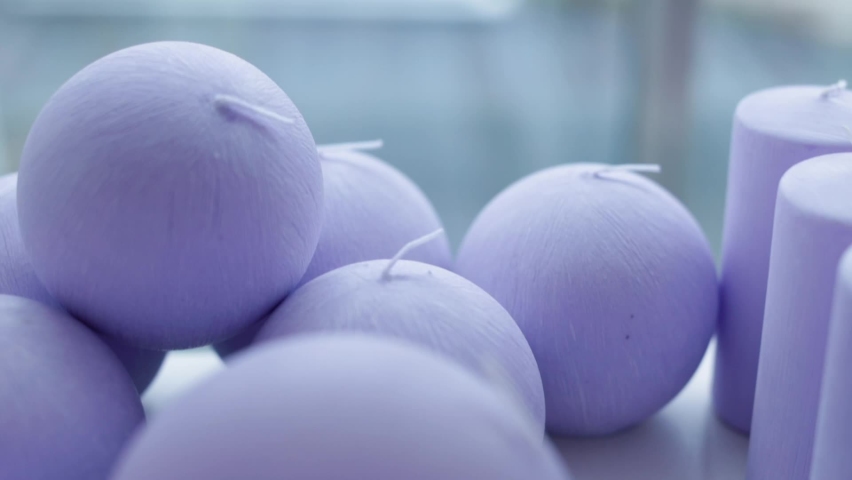 Lilac candles of various round and cylindrical shapes on the shelves look very tactilely attractive. Close-up. The hand takes one of the candle, a selection of a special product.