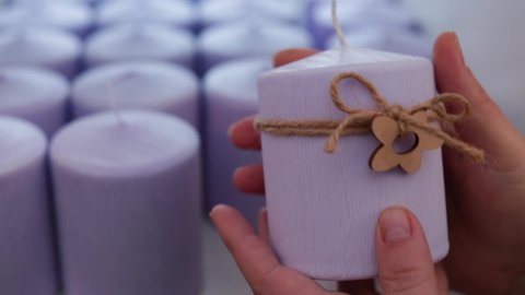 Lilac candles of various round and cylindrical shapes on the shelves look very tactilely attractive. Close-up. The hand takes one of the candle, a selection of a special product.