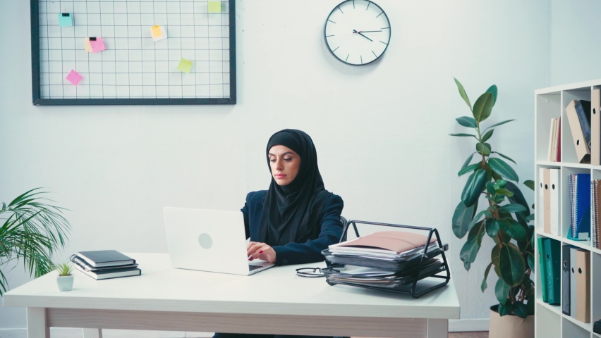 Muslim businesswoman using laptop near papers in office Royalty-Free Stock Footage #1063037254