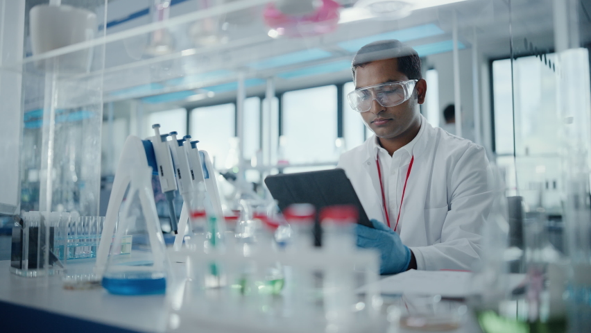 Medical Research Laboratory: Portrait of a Handsome Male Scientist Using Digital Tablet Computer to Analyse Data. Advanced Scientific Lab for Medicine, Biotechnology, Microbiology Development Royalty-Free Stock Footage #1063037674