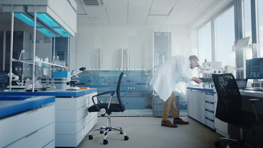 Modern Medical Research Laboratory with Male Scientist Looking Under Microscope, Analysing Microbiological Sample. Advanced Scientific Lab for Drugs, Vaccine Development, Full of High-Tech Equipment | Shutterstock HD Video #1063037830