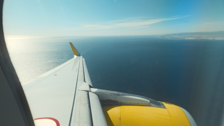 Zoom out from passenger airplane window view on clear blue sky and plane wing with turbine. Passenger or traveller shows thumbs up, allowed to travel after restriction and ban lifted. Destination