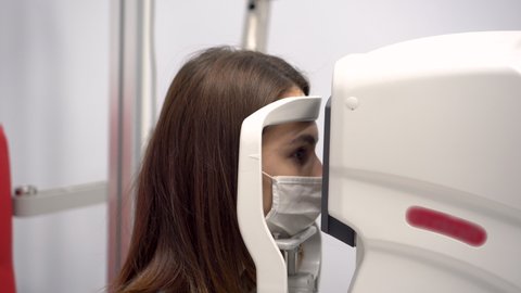 A young woman's eyesight is checked with a special apparatus. The girl wears a protective mask from the virus.
