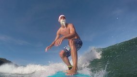 SLOW MOTION CLOSE UP: Cheerful Santa surfer riding fun waves in sunny ocean. Smiling surfer Santa Clause surfing waves towards the shore to wish a Merry Christmas.  - Powered by Shutterstock - Get 15% off with code: PIKWIZARD15