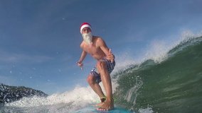 SLOW MOTION CLOSE UP: Cheerful Santa surfer paddling and catching fun waves in sunny ocean. Smiling Santa Clause surfer riding waves towards the shore to wish a Merry Christmas.  - Powered by Shutterstock - Get 15% off with code: PIKWIZARD15
