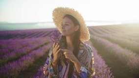 Young woman in a hat with a bouquet of lavender enjoys the scent of herbs. Provence is a beautiful blooming lavender field. Aromatherapy. Slow motion 4K video