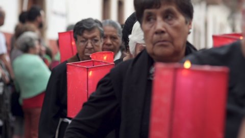 PATZCUARO, MEXICO - APRIL 3, 2015 - Elderly Hispanic woman wearing black walking with red candle holders in a parade during the Silent Procession during Easter's Holy Week celebration