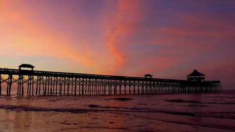 The fishing pier on island of Folly Beach, near Charleston, South Carolina, is silhouetted by a colorful sunrise sky over the Atlantic Ocean in this looping video footage.