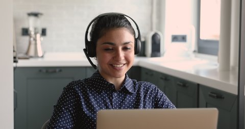Attractive pleasant young mixed race indian woman in wireless headset with microphone holding video call conversation with client or colleagues, discussing working issues or studying on online courses